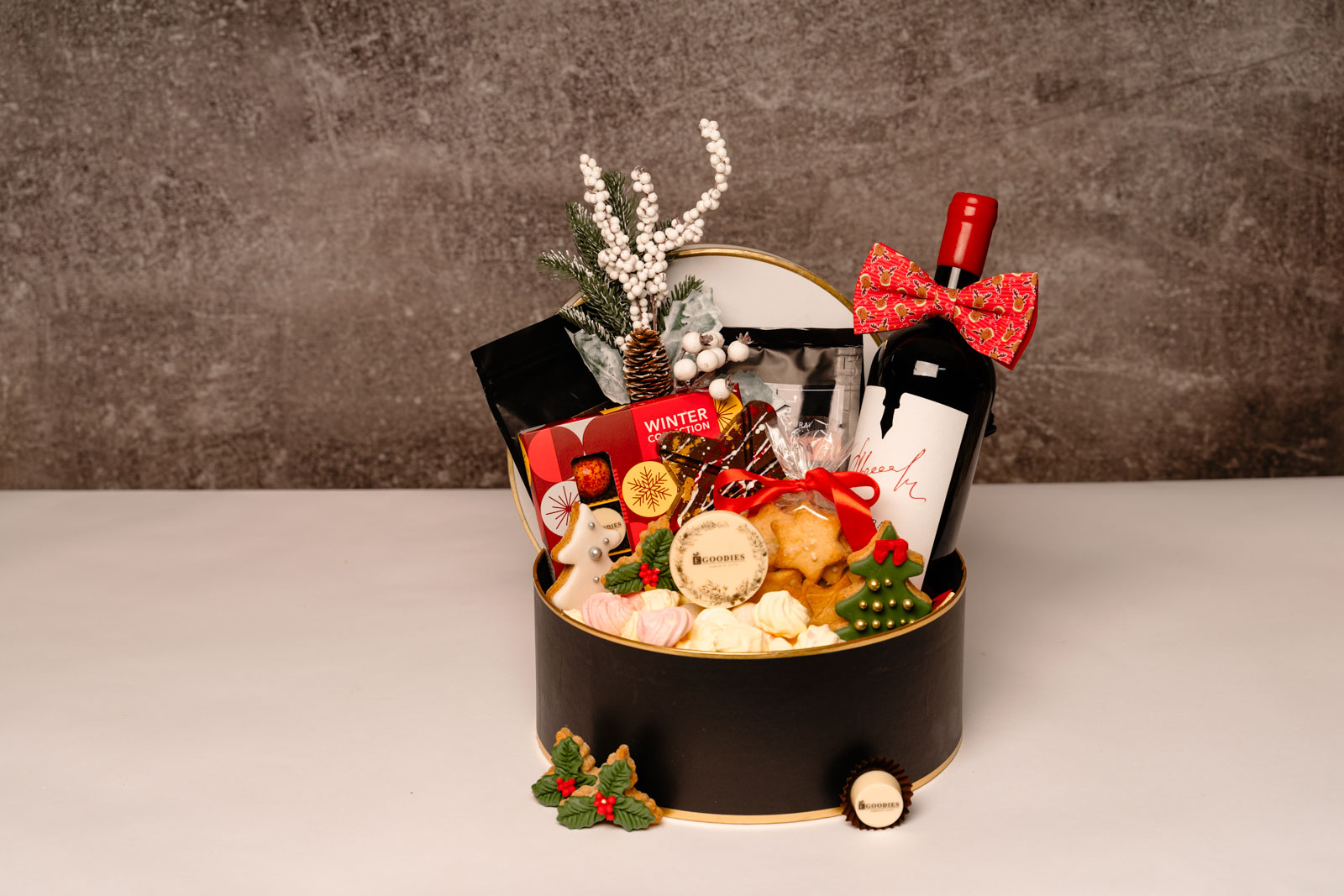 Cadou de Crăciun Egoodies în cutie rotundă neagră: vin roșu cu papion, cafea de specialitate, praline personalizate cu logo, turtă dulce și crenguță cu bobițe albe