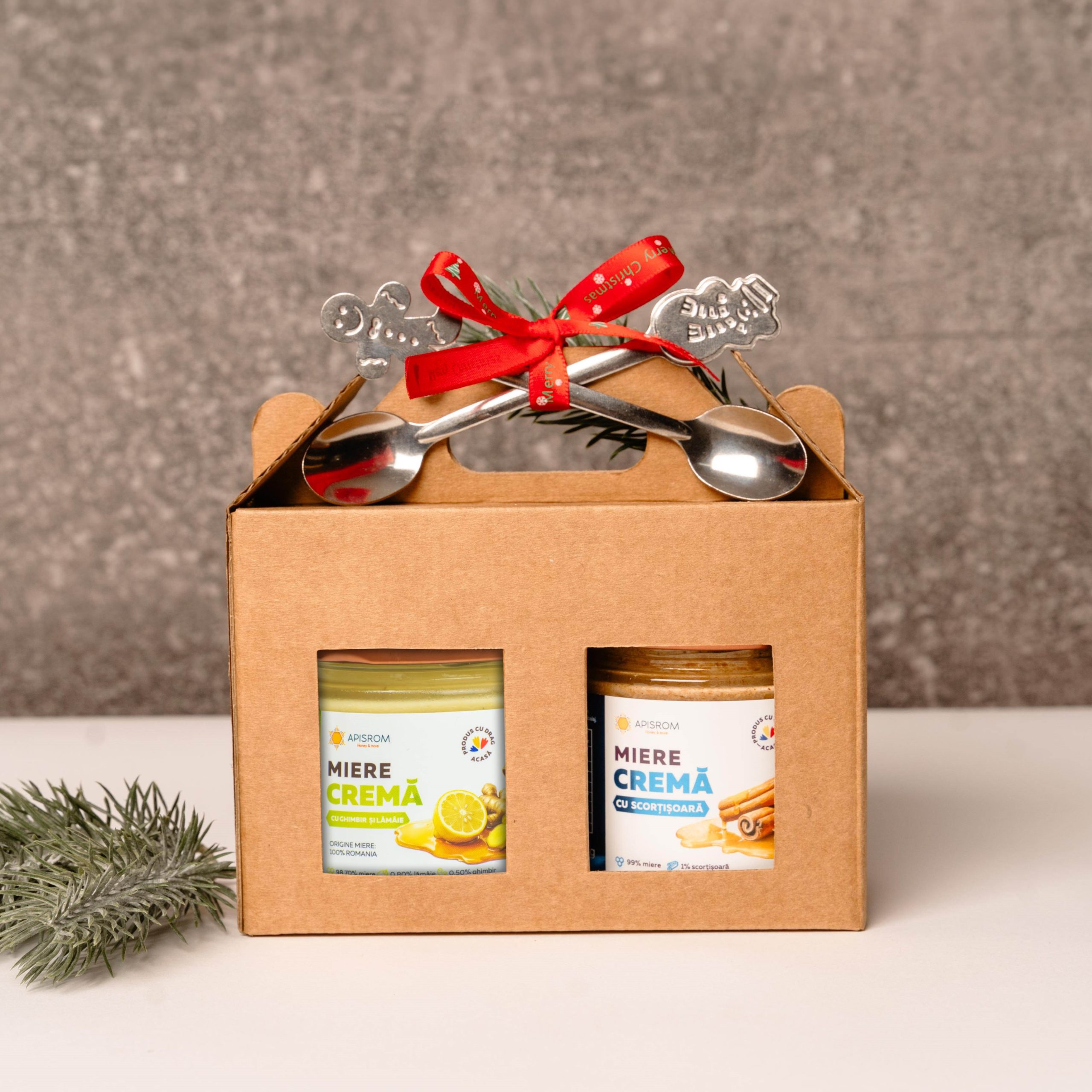 cadou-craciun-miere-ghimbir-scortisoara doua borcane de miere in cutie de carton craft un borcan miere de lamaie ;i ghimbir, un borcan cu miere cu scortisoara, 2 lingurite de inox cu model de Craciun
