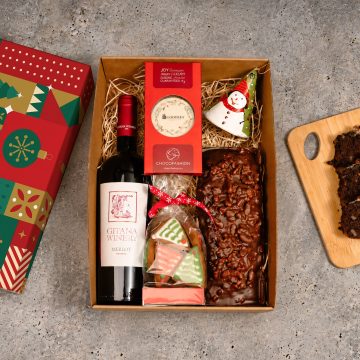 cutie cadou cu sticla de vin rosu cu eticheta alba de la Gitana Winery, ciocolata personalizata cu logo, turta dulce in forma de brazi cu glazura alba si rosie, chec cu ciocolata si nuci, clopotel ceramica, rosu cu desen cu om de zapada