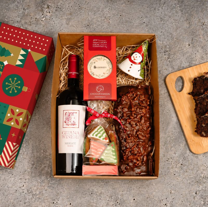 cutie cadou cu sticla de vin rosu cu eticheta alba de la Gitana Winery, ciocolata personalizata cu logo, turta dulce in forma de brazi cu glazura alba si rosie, chec cu ciocolata si nuci, clopotel ceramica, rosu cu desen cu om de zapada