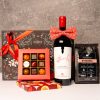 cos cadou Craciun, sticla de vin rosu, autograf de care este prins un papion asortat, rosu, cu model de Craciun, cutie de 9 praline, una personalizata cu logo, punga neagra de cafea de specialitate manufaktura, cutie pentru cadou cu grafica neagra si arabescuri, cu funda rosie, eleganta