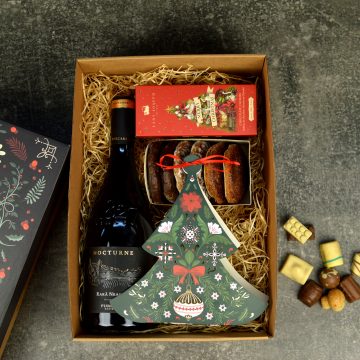 Coș cadou corporate de Crăciun cu vin roșu, dulciuri și decorațiune festivă în formă de brad.