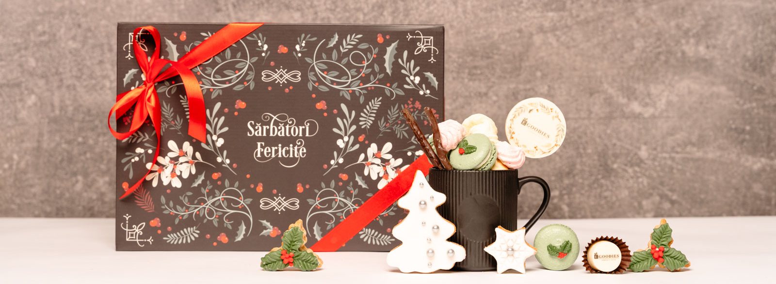 Cutie cadou de Crăciun Egoodies „Sărbători Fericite” cu fundă roșie, alături de o cană cu macarons, bezele și turtă dulce